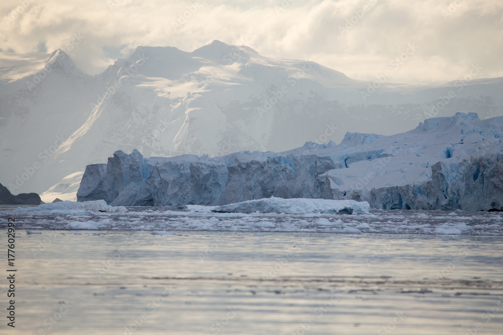 A huge glacier protrudes in to the ocean with a mountain background