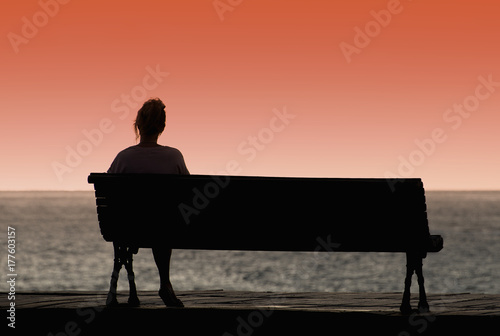 Silhouette of woman sitting alone on the bench in front of the sea