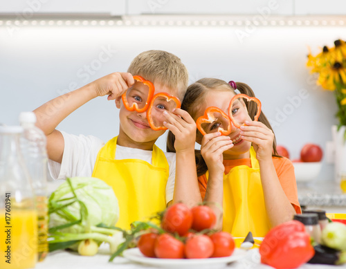 Happy kids having fun with food vegetables at kitchen holds pepper before his...