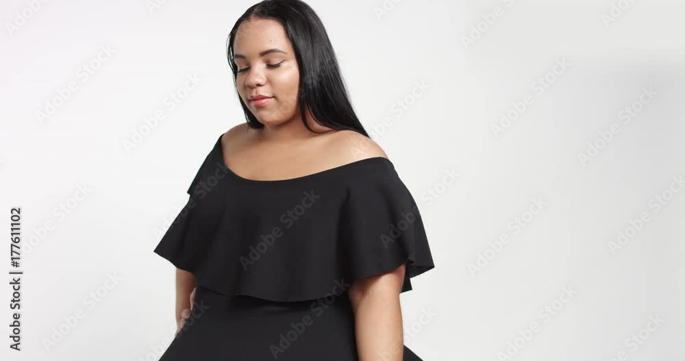 Confident strong young plus size African American model wearing a black short twirly dress flirting with camera isolated on white. touching hair and looking at camera