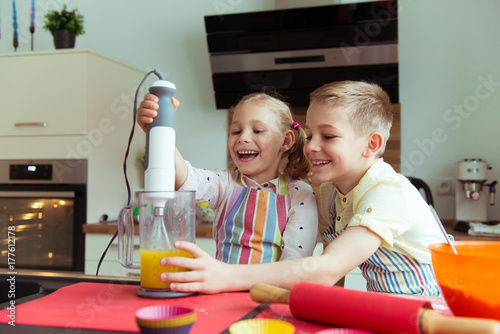 Portrait of two happy and cute little children which having fun during preparing muffins with blender