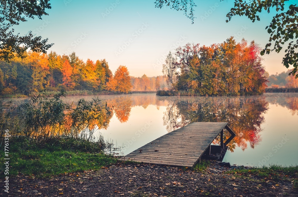 Beautiful autumn landscape. Wooden pier and colorful trees on the lake.