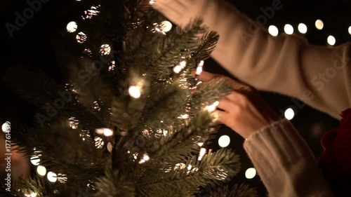 Female decorating the lights on a Christmas tree with bokeh lights background.