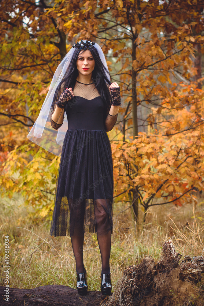 Halloween Witch with magic lights in dark autumn forest. Beautiful young european or american woman in black Gothic dress.Halloween party at city, decor and design for party, mysterious lady in woods Halloween Witch with magic lights in dark autumn forest. Beautiful young european or american woman in black Gothic dress.Halloween party at city, decor and design for party, mysterious lady in woods