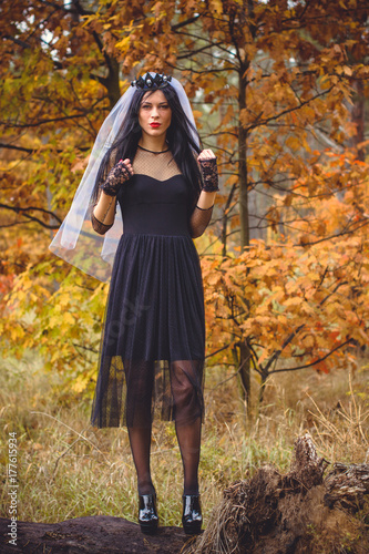 Halloween Witch with magic lights in dark autumn forest. Beautiful young european or american woman in black Gothic dress.Halloween party at city  decor and design for party  mysterious lady in woods