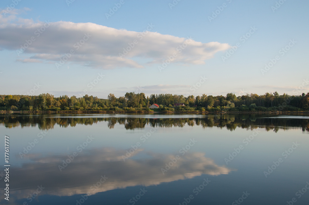 Panorama landscape with a forest and clouds reflecting in water of river Daugava. There is a cottage with red roof in the center