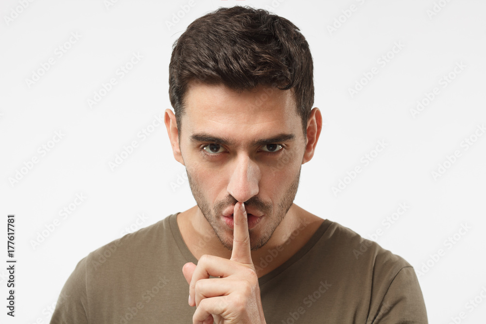 Close up shot of handsome male with shhh gesture, asking for silence or to be quiet, isolated on gray background Close up shot of handsome male with shhh gesture, asking for silence or to be quiet, isolated on gray background