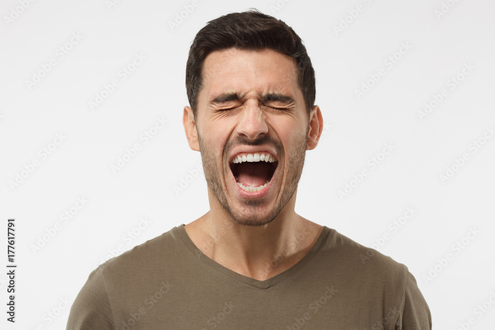Closeup portrait of screaming with closed eyes crazy young man isolated on gray background Closeup portrait of screaming with closed eyes crazy young man isolated on gray background