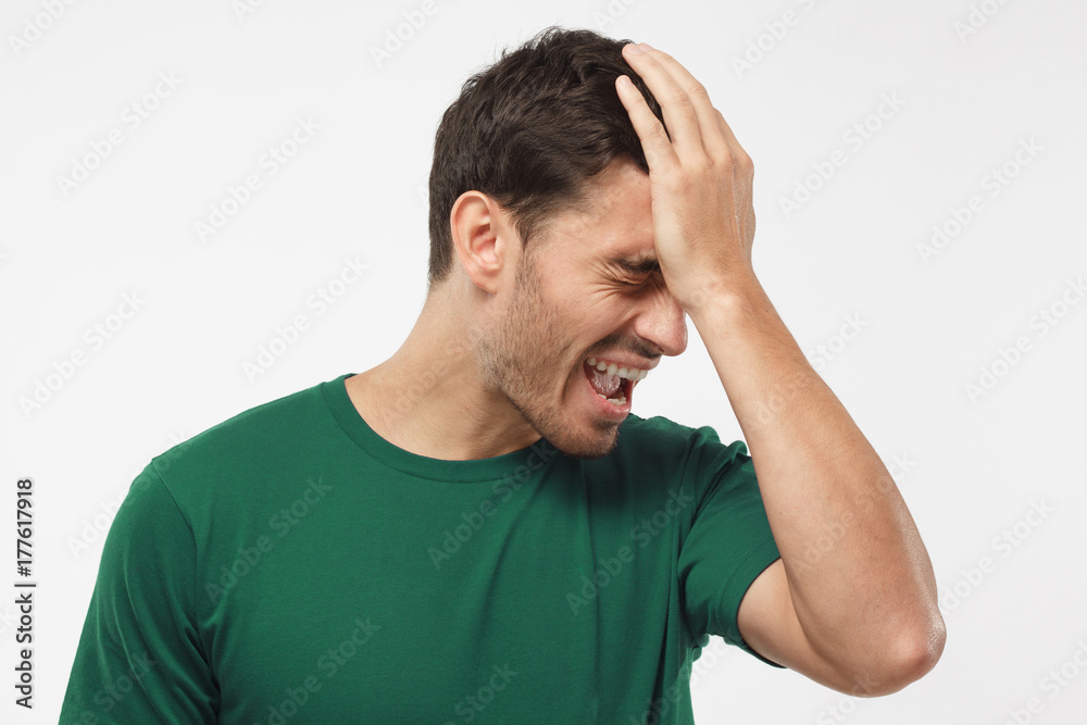 Indoor shot of disappointed stressed out student in green t-shirt making facepalm with hand. His team lose soccer match and cup. Indoor shot of disappointed stressed out student in green t-shirt making facepalm with hand. His team lose soccer match and cup.