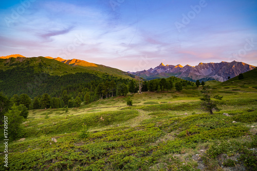 The Italian Alps at sunset. Summer colorful sky over the majestic mountain peaks, woodland and green valleys.