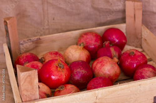 Ripe red pomegranates in a wooden box on brown burlap