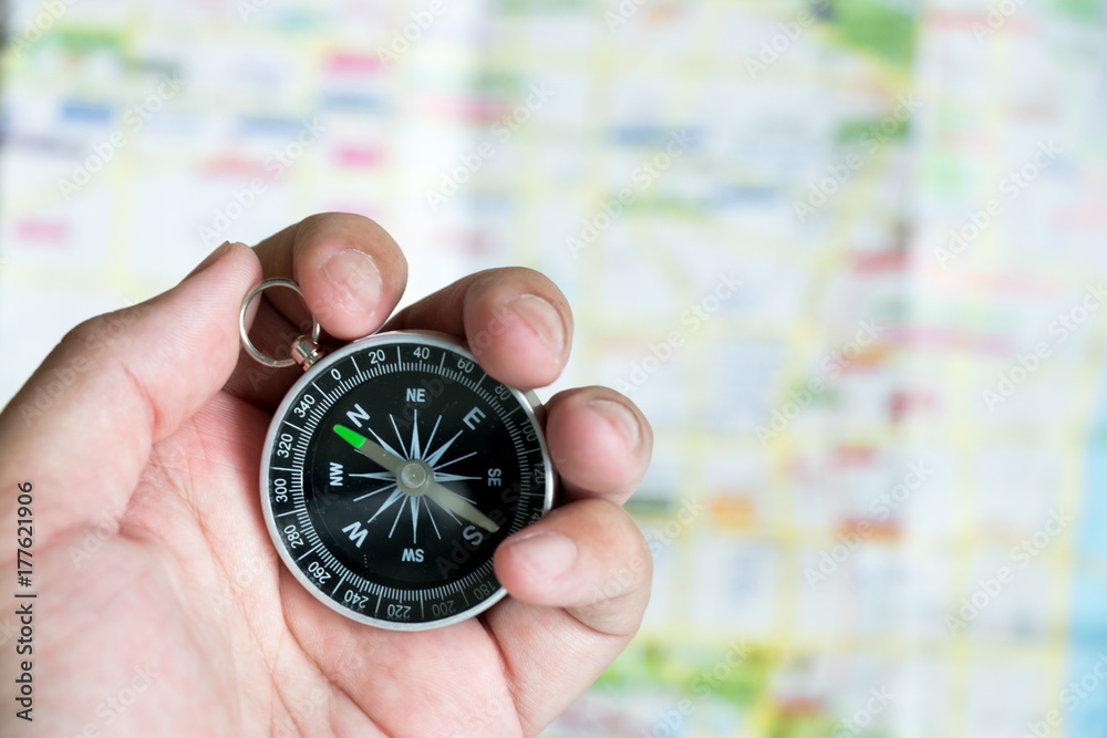 Man hold compass to check the direction with blurred map