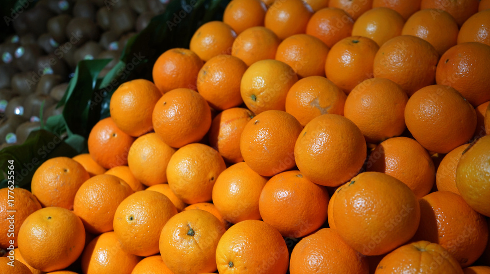 Pile of oranges on the counter in supermarket, green kiwifruit in background