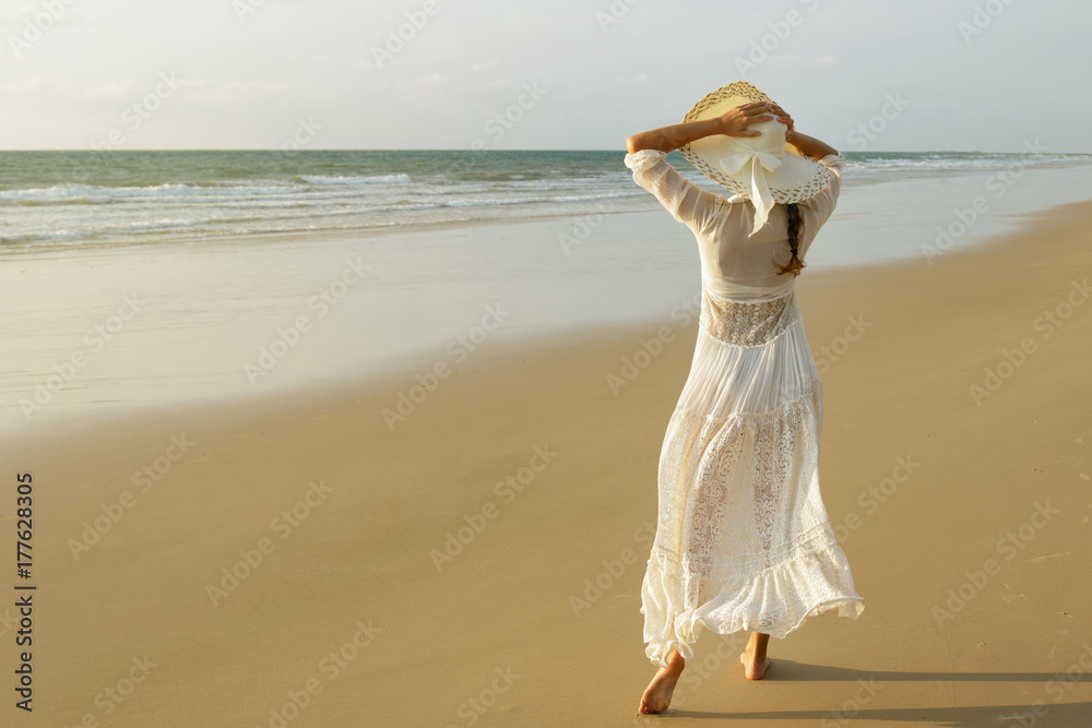 Woman wearing beautiful white dress is walking on the beach during sunset Woman wearing beautiful white dress is walking on the beach during sunset