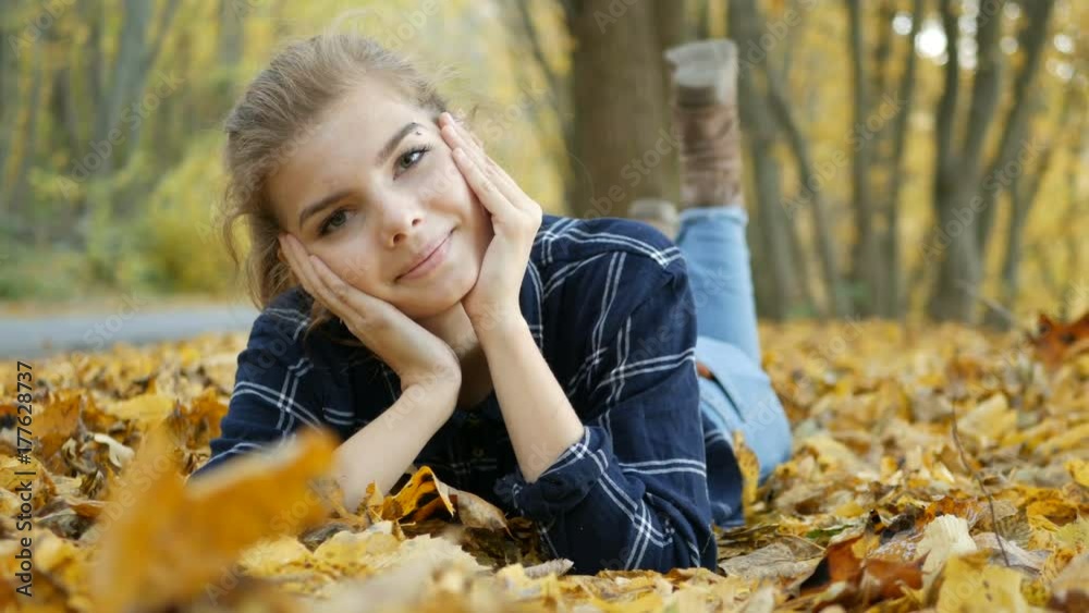 Young beautiful girl in blue jeans lying on yellow leaves, in the autumn park Young beautiful girl in blue jeans lying on yellow leaves, in the autumn park