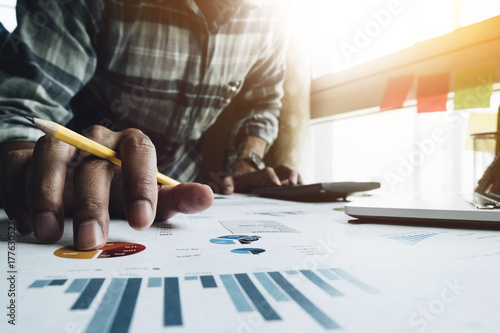 Close up of businessman or accountant hand holding pencil working on business document report and calculator to calculate business data, accountancy document and laptop computer at office 