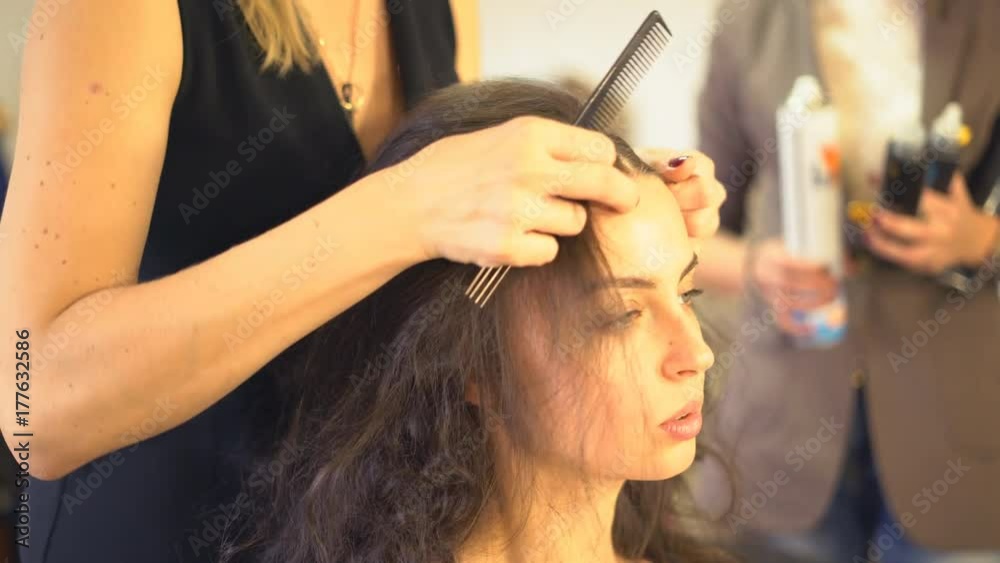hair styling in the beauty salon. A professional hair stylist makes a haircut for the model with a comb. A woman is sitting in a chair in a beauty salon. young attractive brunette preparing for the