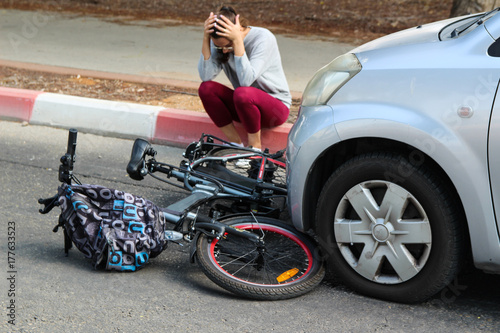 A woman holding her head near a traffic accident between electric e bike and car