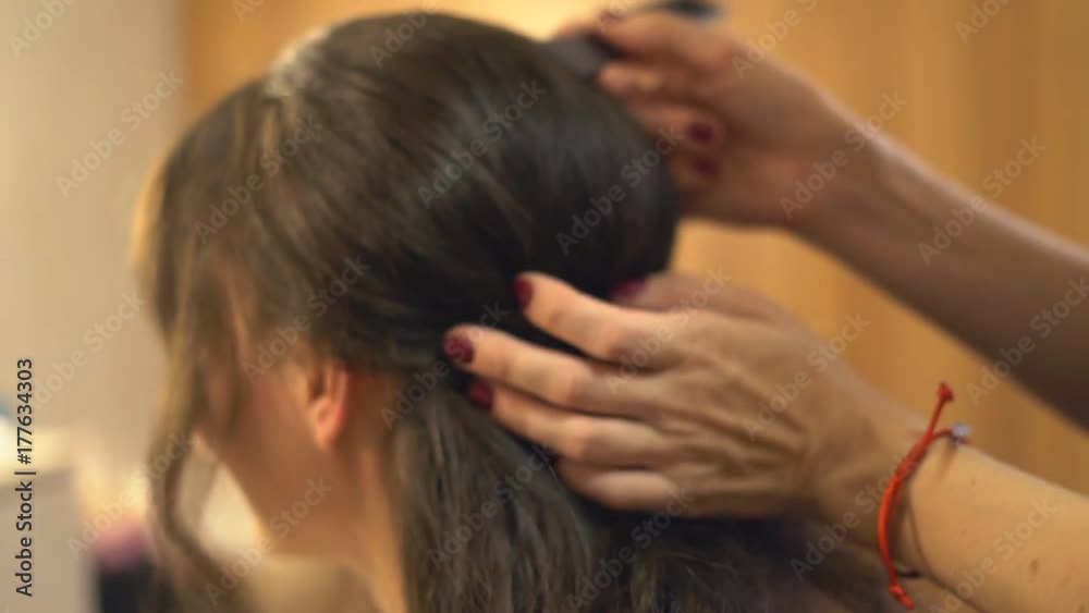 hair styling in the beauty salon. A professional hair stylist makes a haircut for the model with a comb. A woman is sitting in a chair in a beauty salon. young attractive brunette preparing for the hair styling in the beauty salon. A professional hair stylist makes a haircut for the model with a comb. A woman is sitting in a chair in a beauty salon. young attractive brunette preparing for the