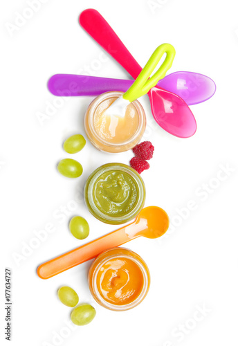 Jars with different baby food and spoons on white background