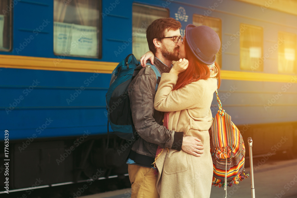 Encounter after a travel of a happy couple hugging in the street in a train station. Beautiful evening warm sunlight