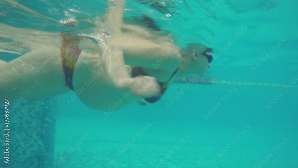 Slow motion shot of pregnant woman in goggles swimming in the pool. Underwater view. Healthy pregnancy