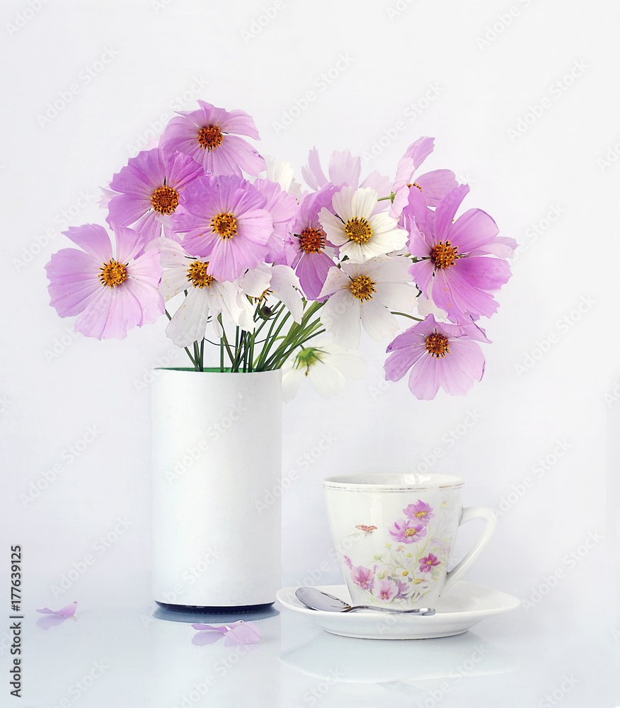 Pink flowers in a white vase and a cup of coffee near it on a white background Pink flowers in a white vase and a cup of coffee near it on a white background