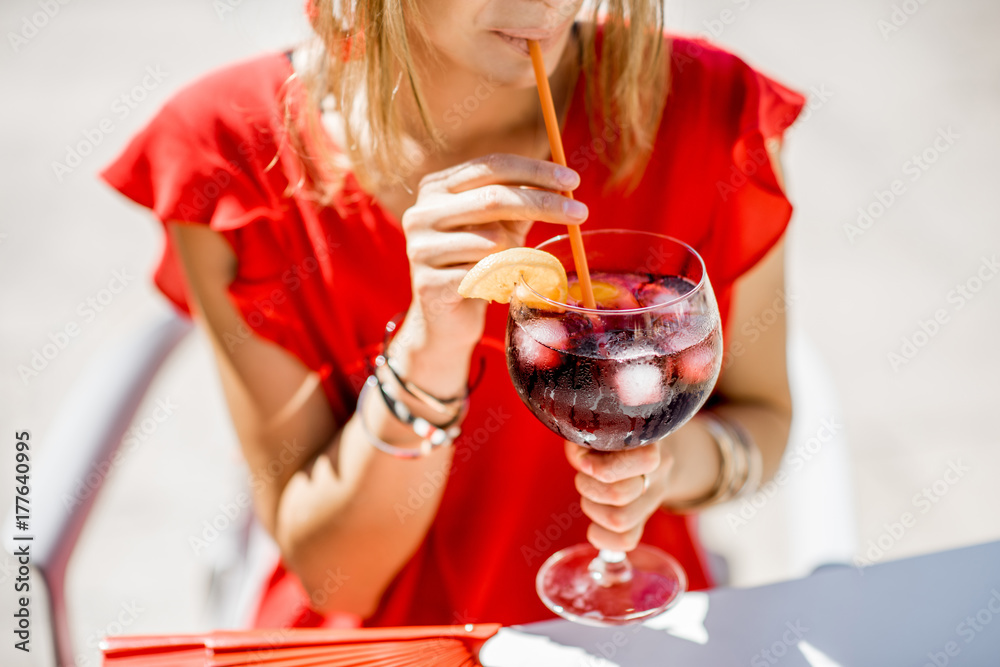 Woman holding a glass with Sangria, traditional spanish alcohol beverage made of wine, sitting outdoors at the restaurant. Image with no face focused on the glass Woman holding a glass with Sangria, traditional spanish alcohol beverage made of wine, sitting outdoors at the restaurant. Image with no face focused on the glass