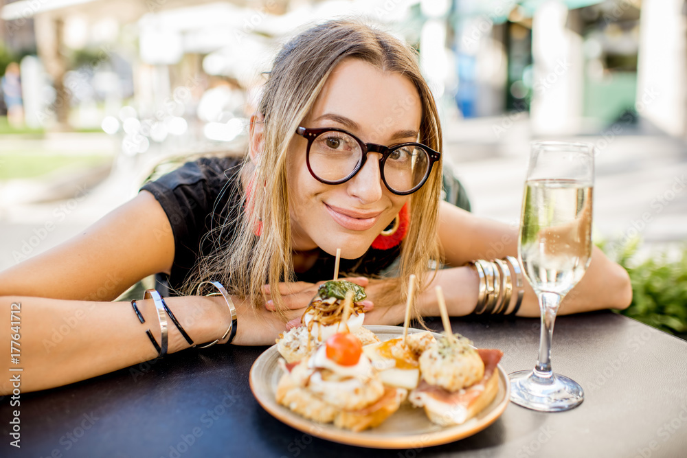 Young woman enjoying tasty appetizer with pinchos, traditional spanish snack, and glass of wine sitting outdoors at the bar in Valencia city