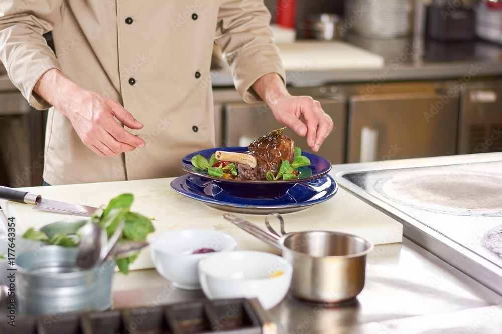 Male chef and lamb shank with vegetables. Chef at professional kitchen cooked lamb shank with vegetables ratatouille. Delicious dish at european restaurant.