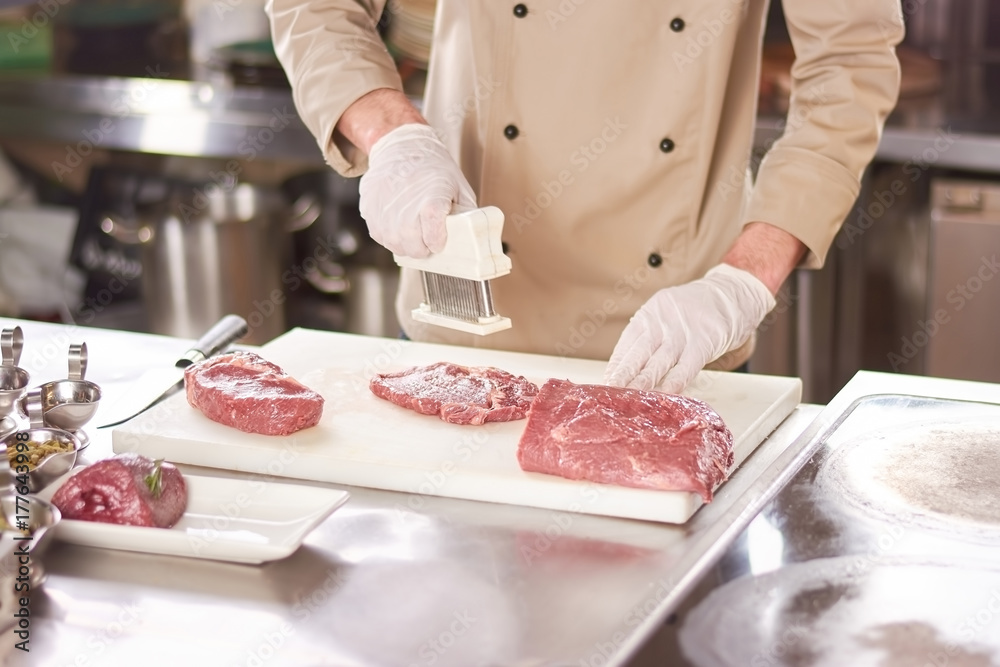 Chef cooking steak at restaurant kitchen. Cook preparing steak from raw beef meat. Chef working at restaurant kitchen.