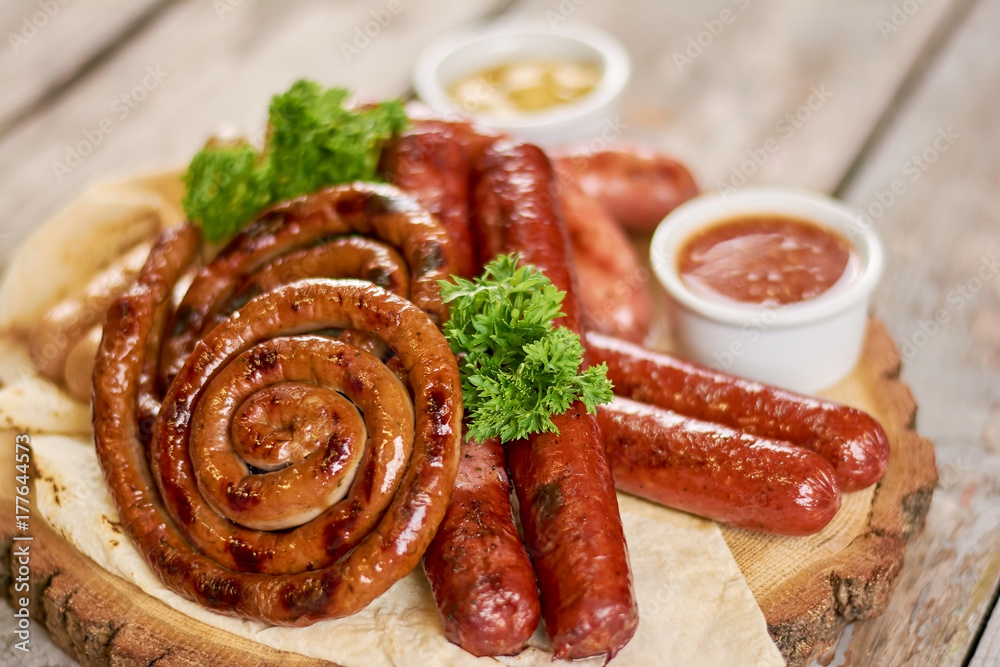 Variety of delicious grilled sausages. Hot grilled sausages with parsley and tasty sauce close up. Appetizing snack for beer.