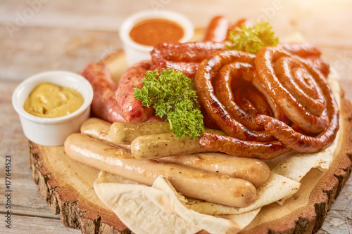 Tasty grilled sausages on wooden board. Assortment of grilled sausages served with parsley. Delicious german food. photo