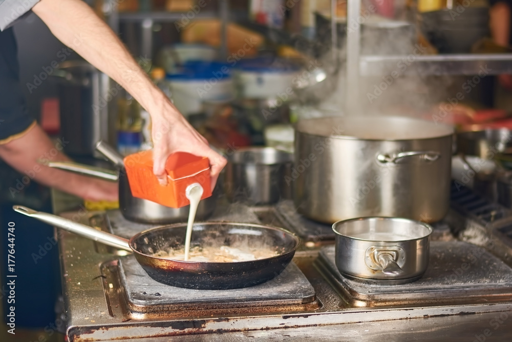 Man pouring milk into frying pan. Man preparing dinner at home kitchen. Man cooking dish with milk at home.