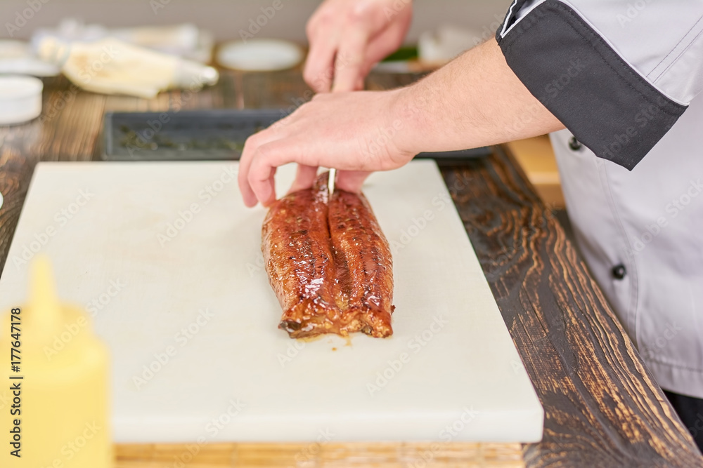 Chef hands slicing eel on cutting board. Male hands cutting fresh eel on white cutting board. Chef at work, kitchen.