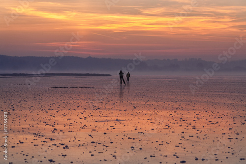 skaters with ski sticks run on the first ice in frosty fog at sunset