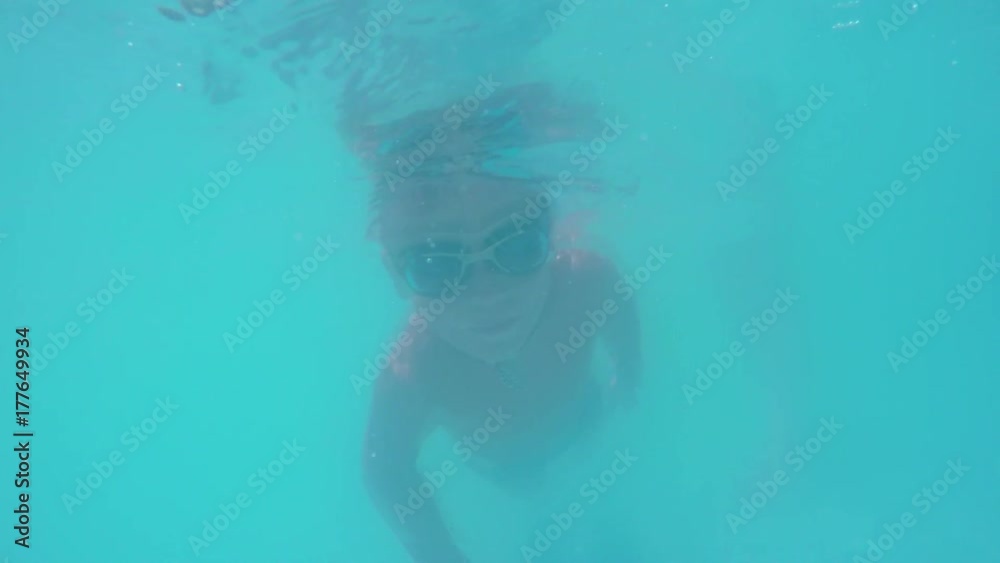 Underwater shot of a boy in goggles diving in the pool and looking to the camera Underwater shot of a boy in goggles diving in the pool and looking to the camera