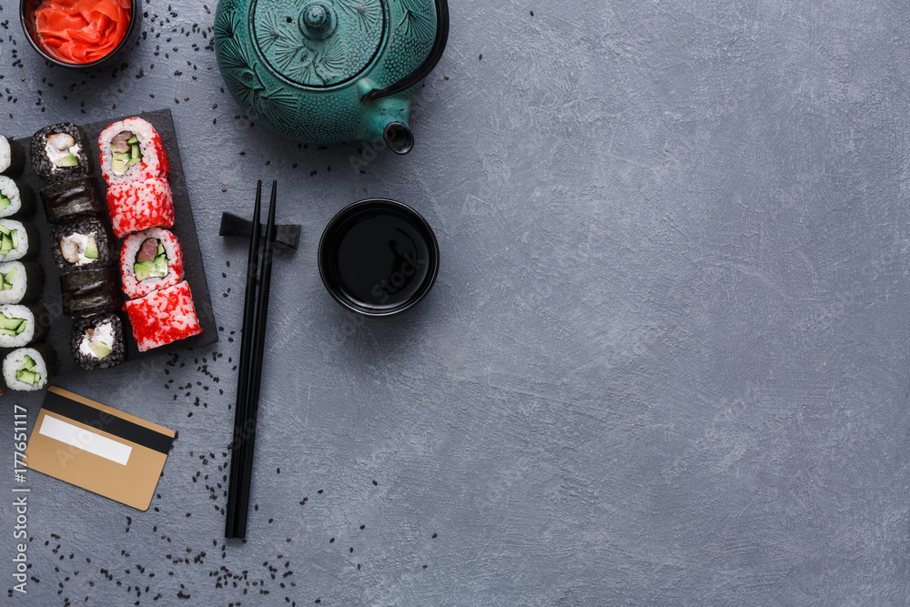 Top view set of sushi maki and rolls with teapot and credit card on rustic grey and sesame background Top view set of sushi maki and rolls with teapot and credit card on rustic grey and sesame background