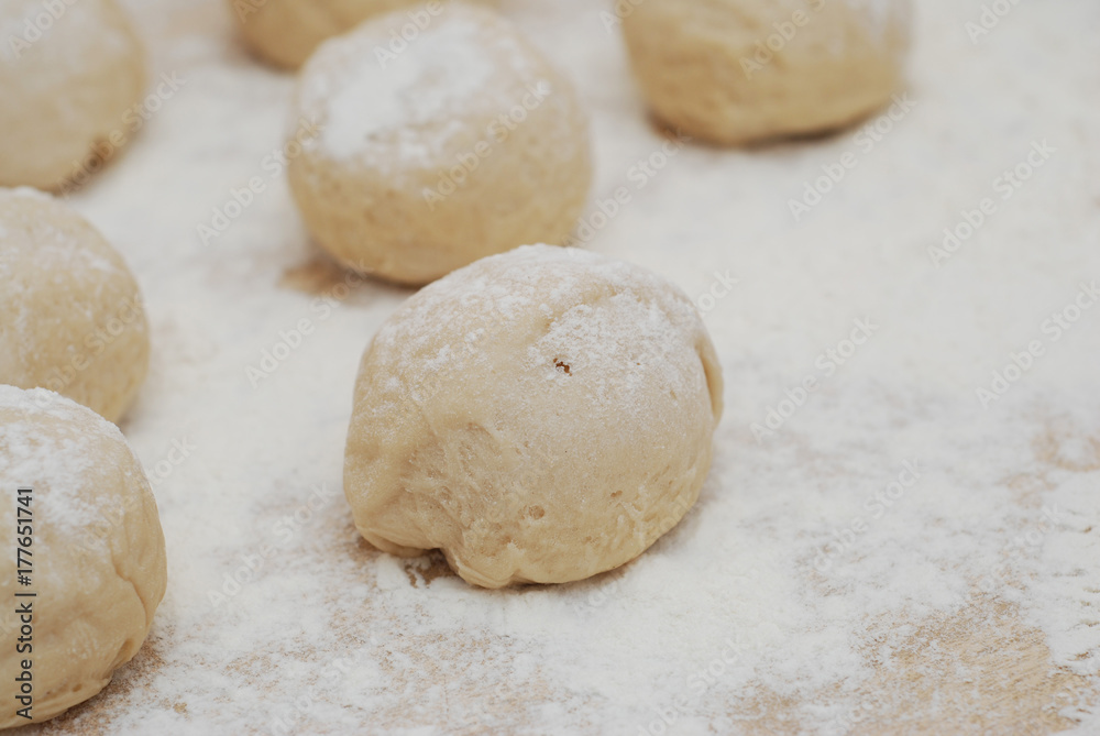 Dough balls made for cooking pastries with flour on the table