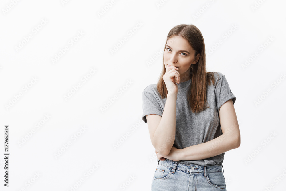 Close up portrait of beautiful dark-haired caucasian young woman with long hair in grey t shirt and jeans lookin in camera with thoughtful face expression, smiling, holding hand near mouth, posing for Close up portrait of beautiful dark-haired caucasian young woman with long hair in grey t shirt and jeans lookin in camera with thoughtful face expression, smiling, holding hand near mouth, posing for