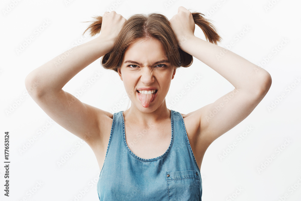 Close up of funny attractive caucasian young student girl looking in camera, showing tongue, making silly faces, having fun. Woman playing with little kid, holding hair and making funny faces to make Close up of funny attractive caucasian young student girl looking in camera, showing tongue, making silly faces, having fun. Woman playing with little kid, holding hair and making funny faces to make