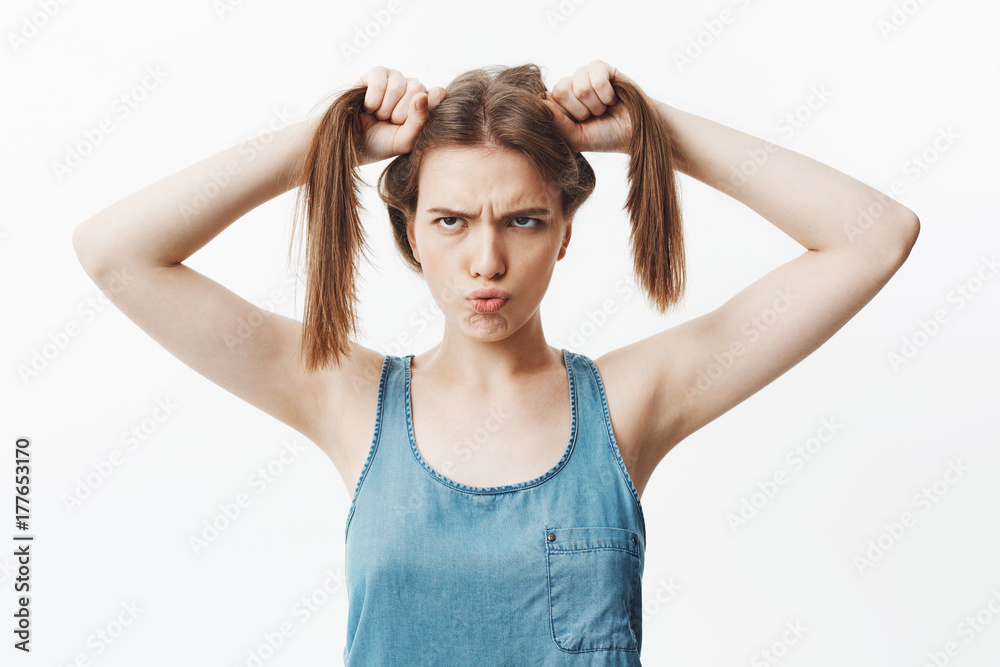 Portrait of funny handsome charming european girl with dark straight hair mowing eyes, holding hair with both hands, having funny and awkward look. Positive emotions and expressions Portrait of funny handsome charming european girl with dark straight hair mowing eyes, holding hair with both hands, having funny and awkward look. Positive emotions and expressions