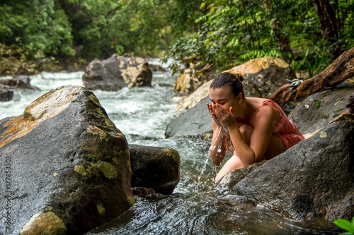 the girl drinks water from a mountain stream