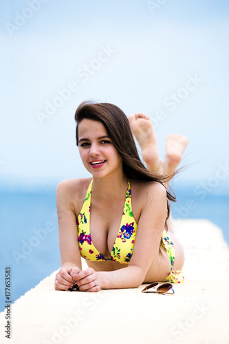 Relaxing young woman on pier at the sea in summer day. Skinny girl in swimsuits posing near sea.