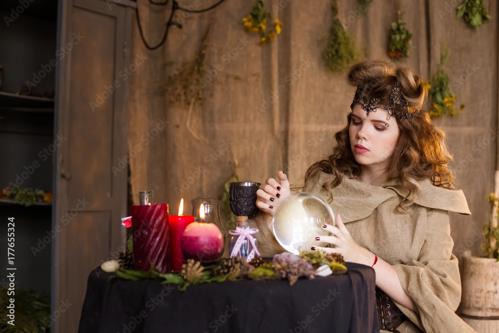 Fototapeta premium A beautiful, sweet teenage girl, the woman of the witch. Magic drink, crystal ball. Little sorceress, herbalist. Divination, home meditsina. Halloween