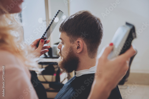 Master cuts hair and beard of men, hairdresser makes hairstyle for a young man. Hipsters