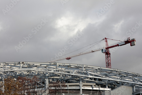 Construction crane against the gray sky. The red and white mechanism is illuminated by the sun.Diagonal placement in the frame of a construction crane and metal structures