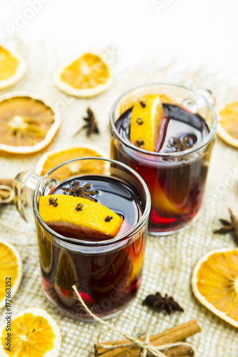 two transparent cups with hot mulled wine and an orange slice among spices of cinnamon and anise