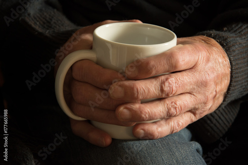 Hands of an old man holding a mug