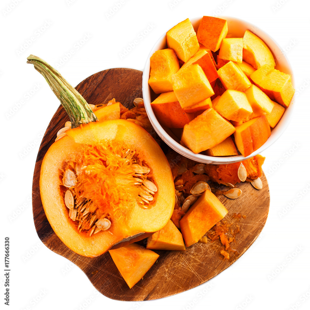 Pumpkin cut in a pieces on wooden cutting board isolated on white background. Diced Pumpkin. Thanksgiving day or seasonal autumnal concept Pumpkin cut in a pieces on wooden cutting board isolated on white background. Diced Pumpkin. Thanksgiving day or seasonal autumnal concept